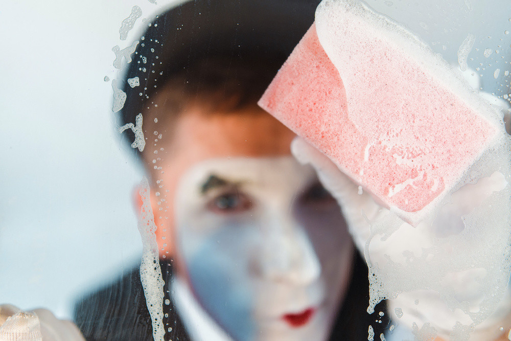Mime cleaning glass with sponge. Shallow depth of field.