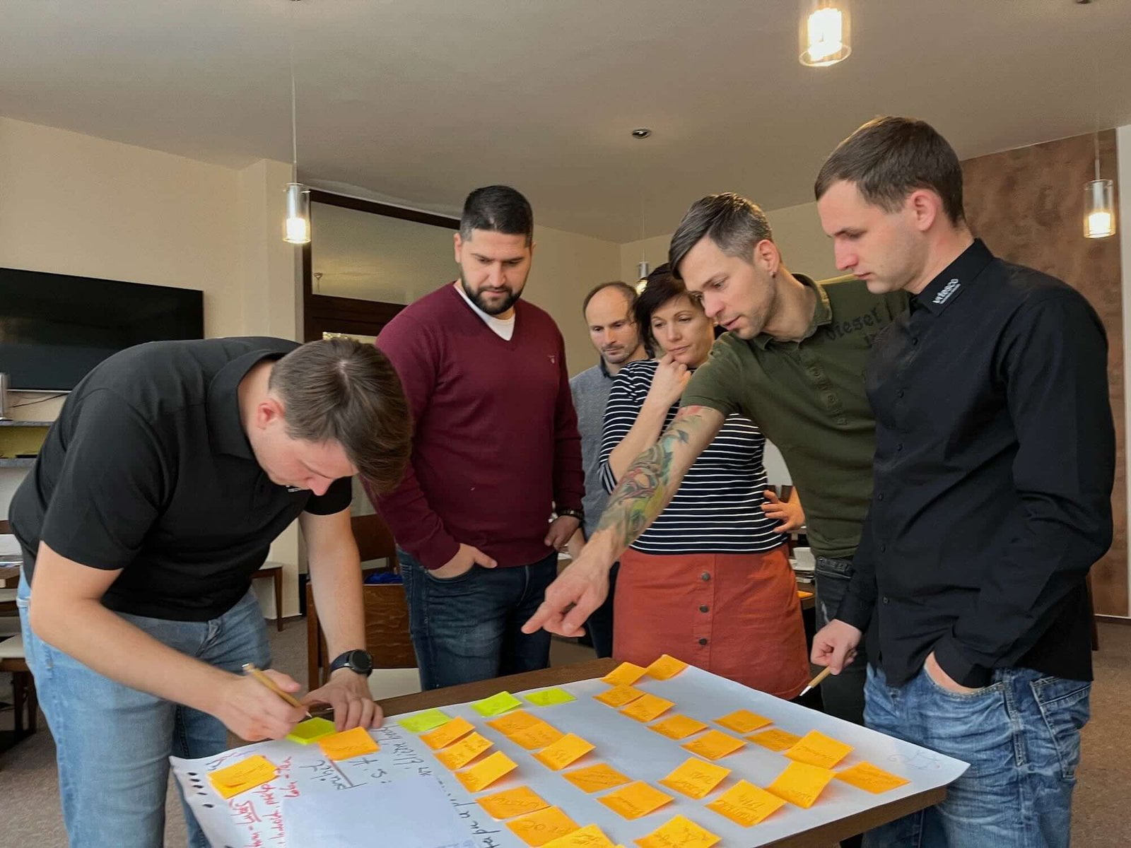 Skupina lidí spolupracuje nad flipchartem pokrytým post-it papírky během tréninku projektového řízení.